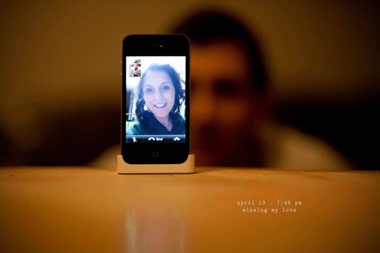 A phone on a table shows a smiling woman on a video call, captioned missing my love.