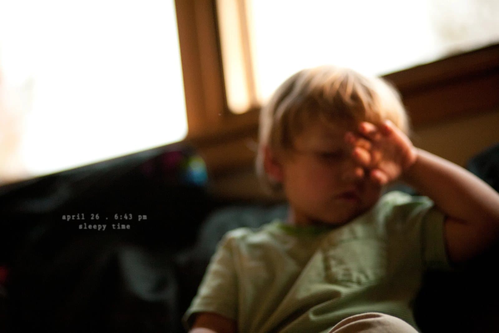 A sleepy toddler rubs his eyes on a couch, captioned sleepy time.