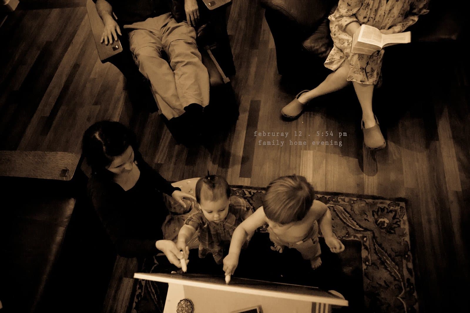 Overhead sepia view of a family on the floor, two toddlers drawing, captioned family home evening.