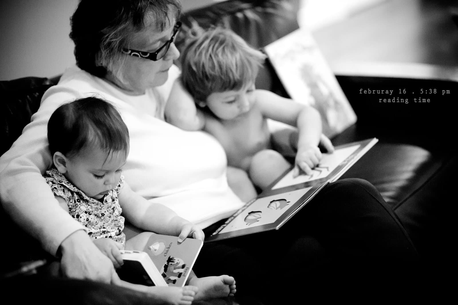 A grandmother reads a picture book to a baby and a toddler on a couch, captioned reading time.