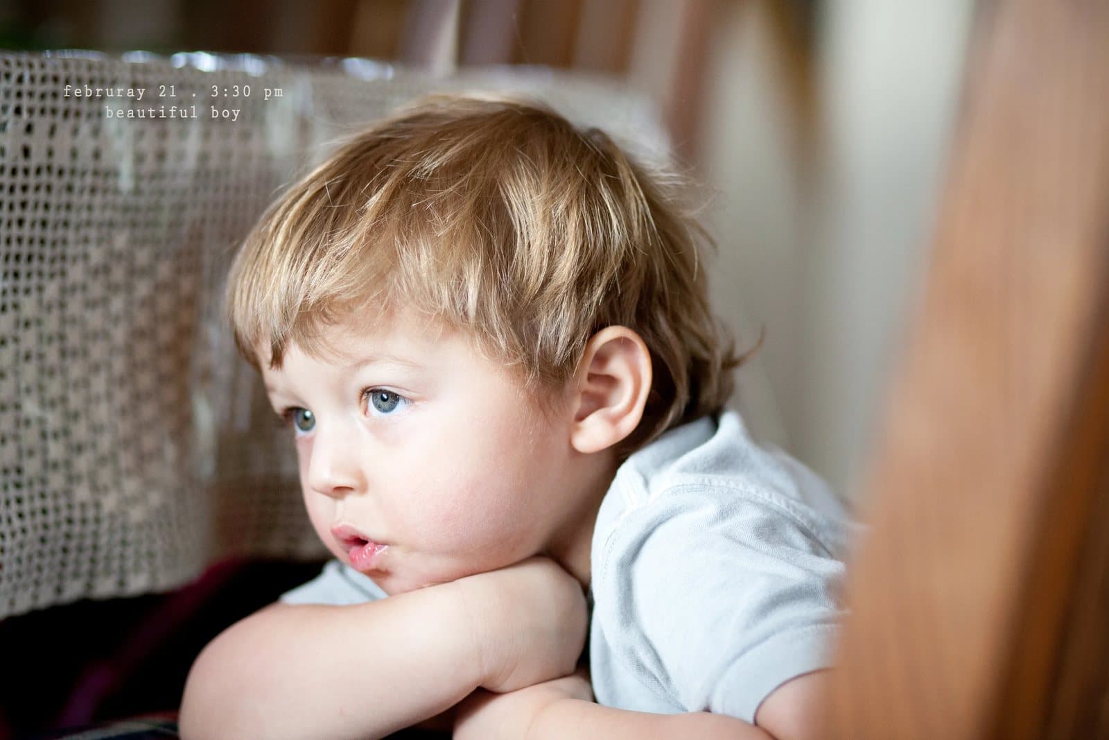 A blond toddler rests his chin on his arms, gazing out, captioned beautiful boy.