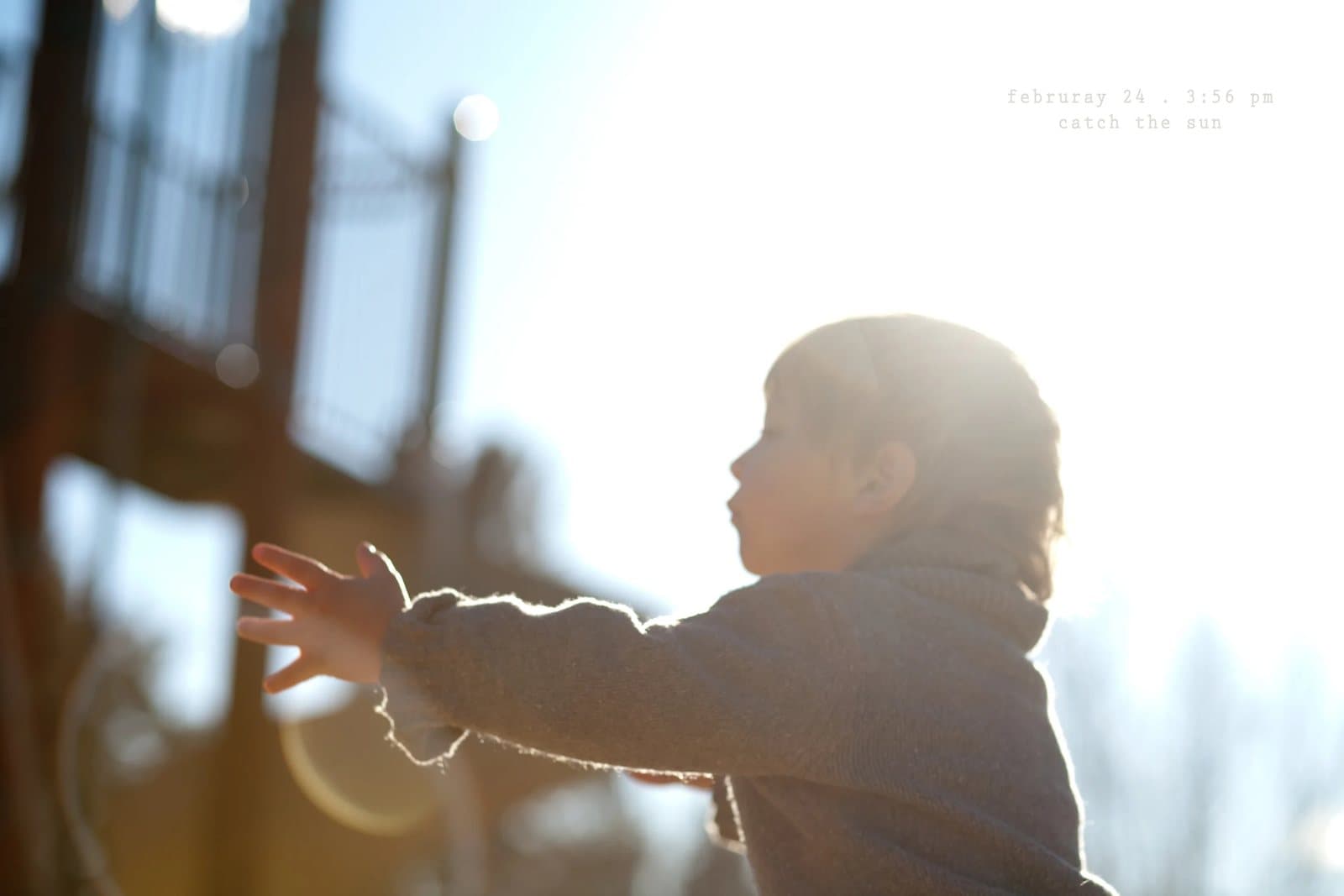 A backlit toddler reaches out toward the sun on a deck, captioned catch the sun.