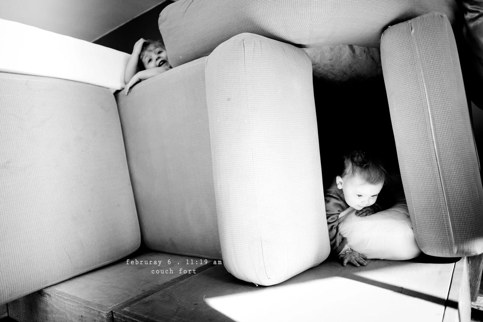 Two children play inside a fort made of couch cushions, captioned couch fort.