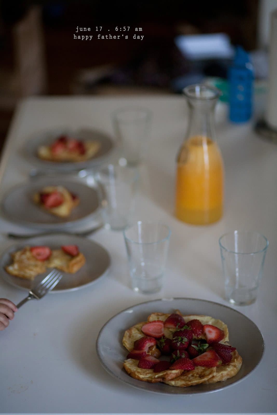 A table set with strawberry pancakes and orange juice, captioned happy father's day.