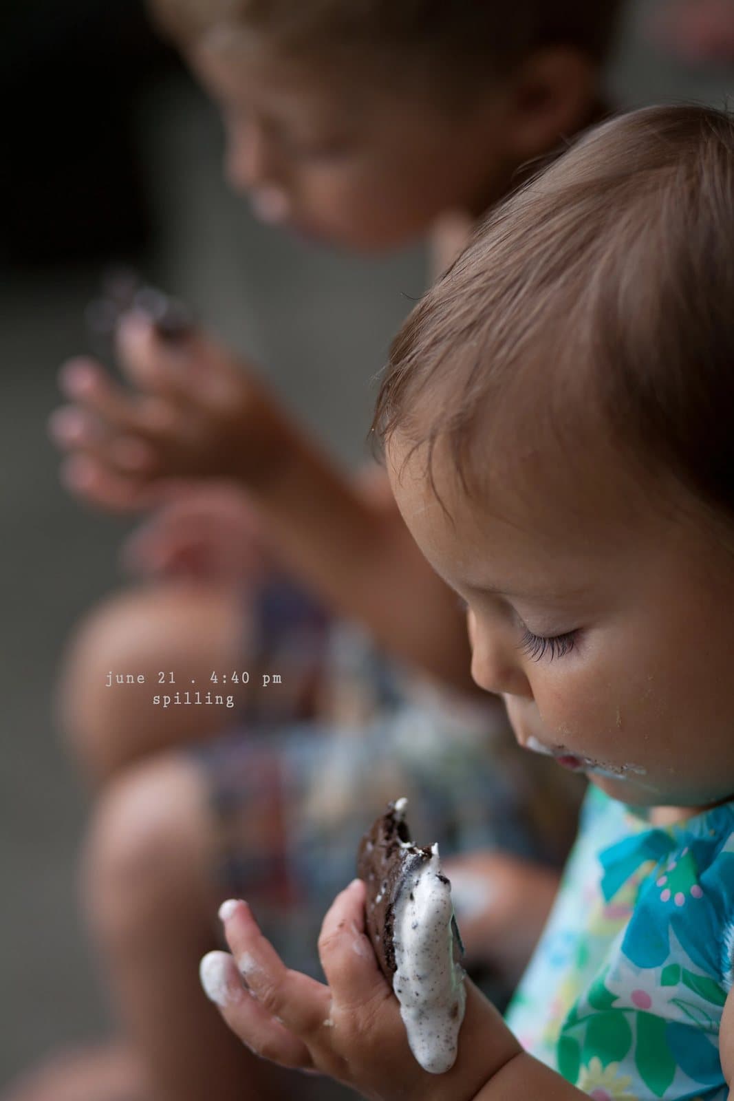 A baby with a messy face holds a half-eaten ice cream sandwich, captioned spilling.
