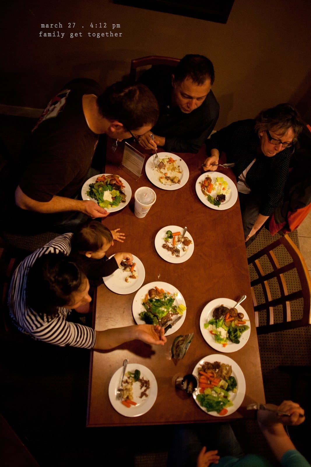 Overhead view of family members sharing salads around a table, captioned family get together.