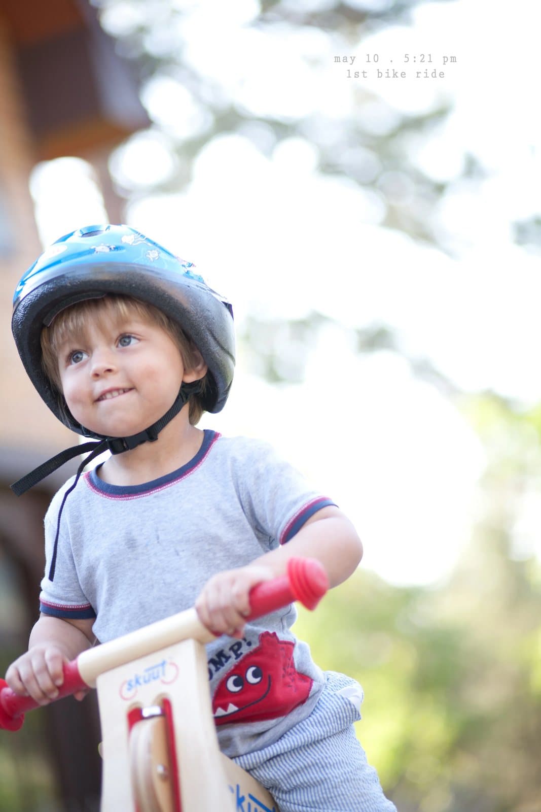 A smiling toddler in a helmet rides a wooden balance bike, captioned 1st bike ride.