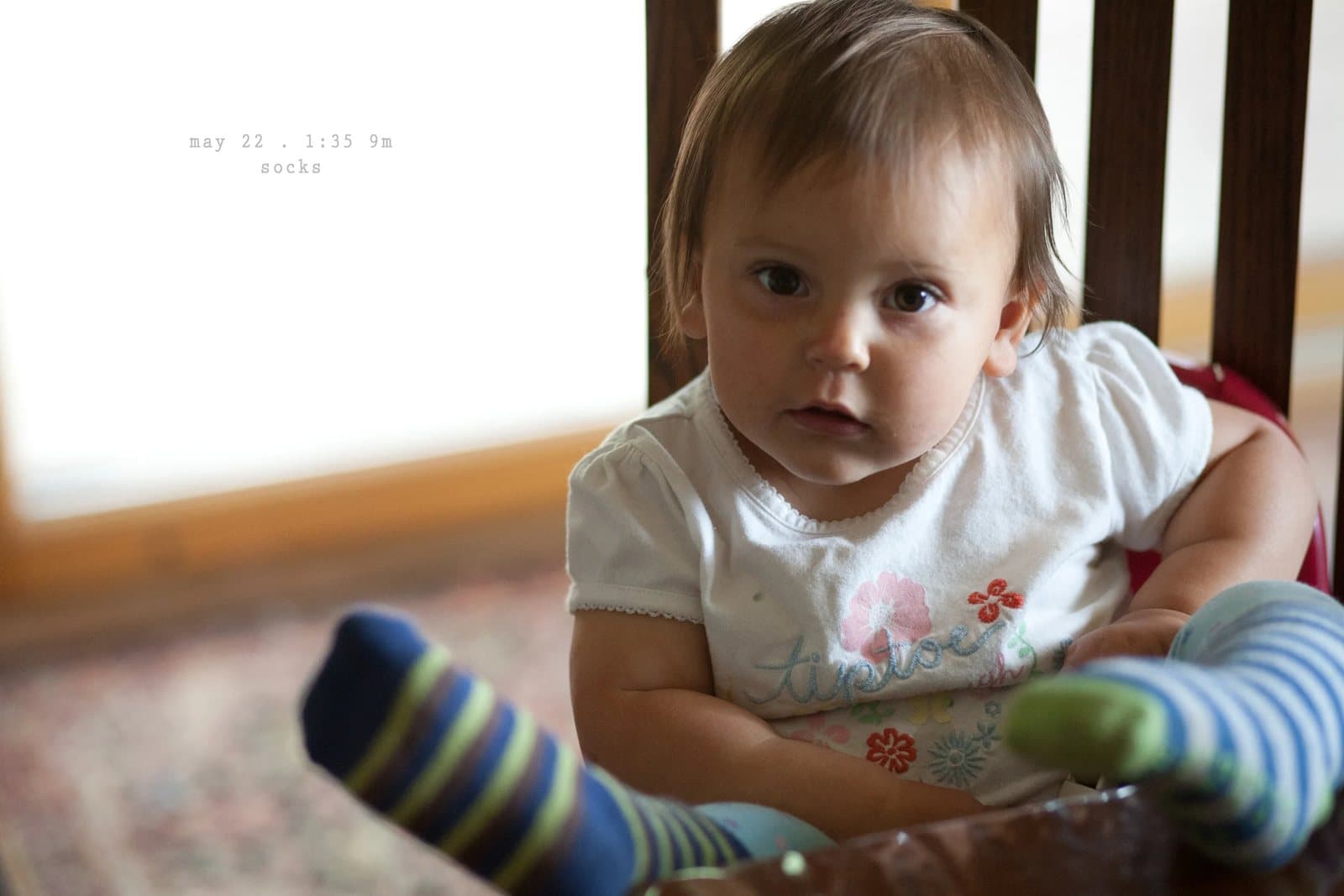 A baby in striped socks sits in a high chair looking at the camera, captioned socks.