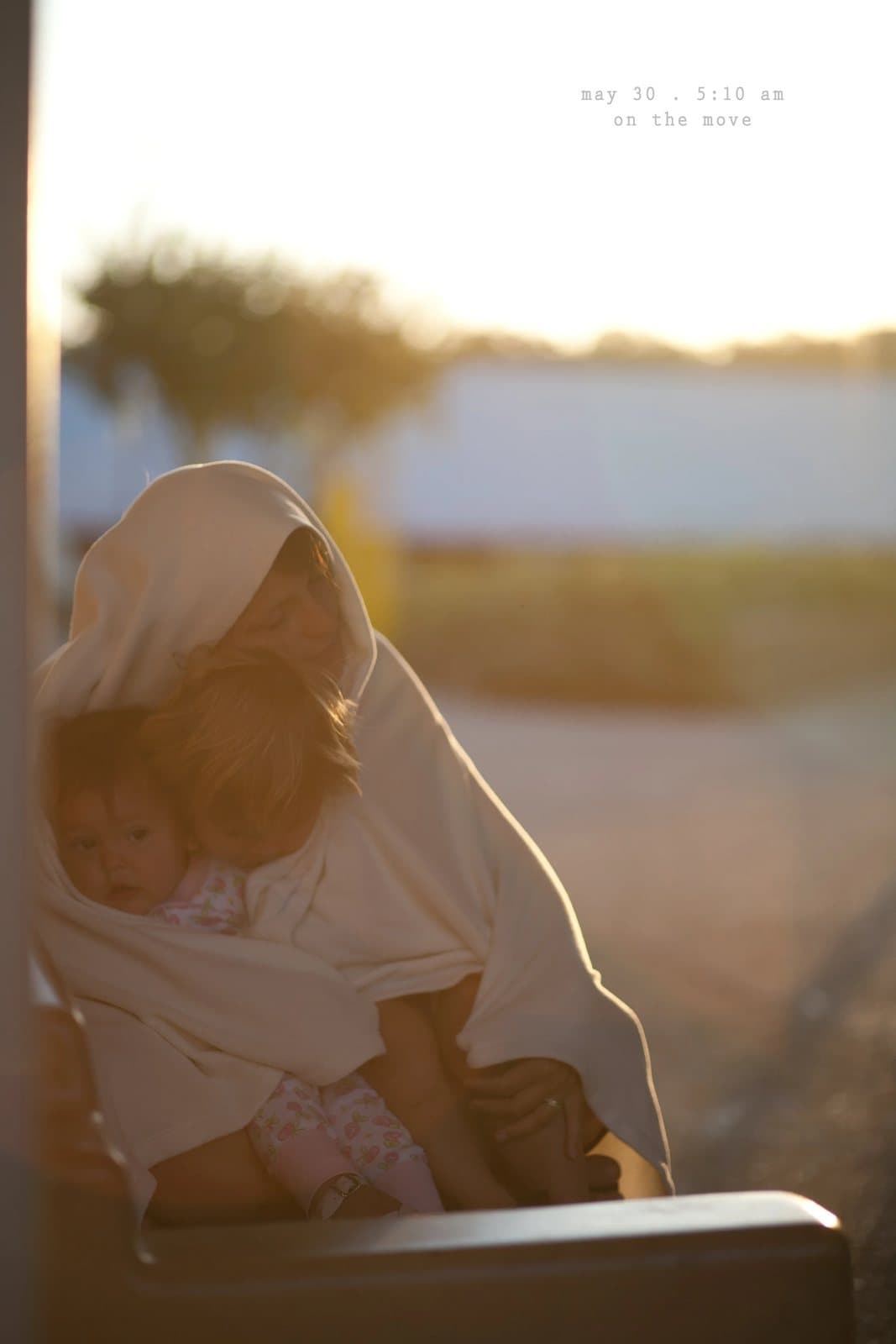 A woman wrapped in a shawl holds a child in golden light, captioned on the move.