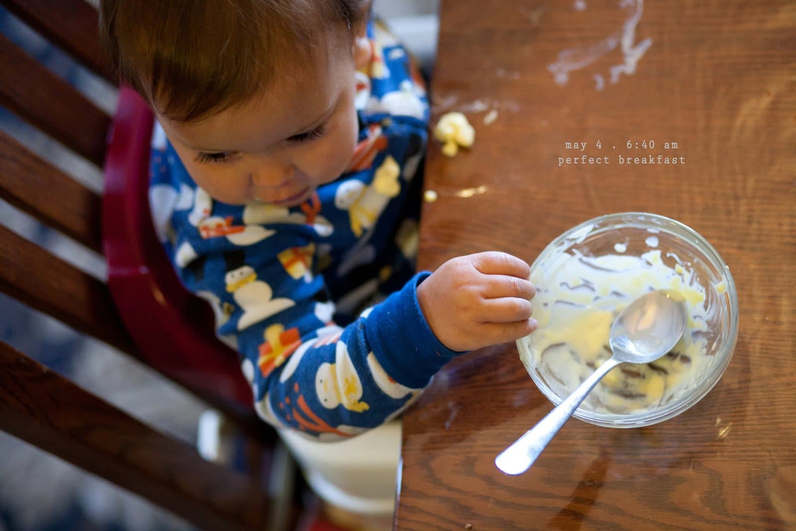 A baby in pajamas eats from a bowl at the table, captioned perfect breakfast.
