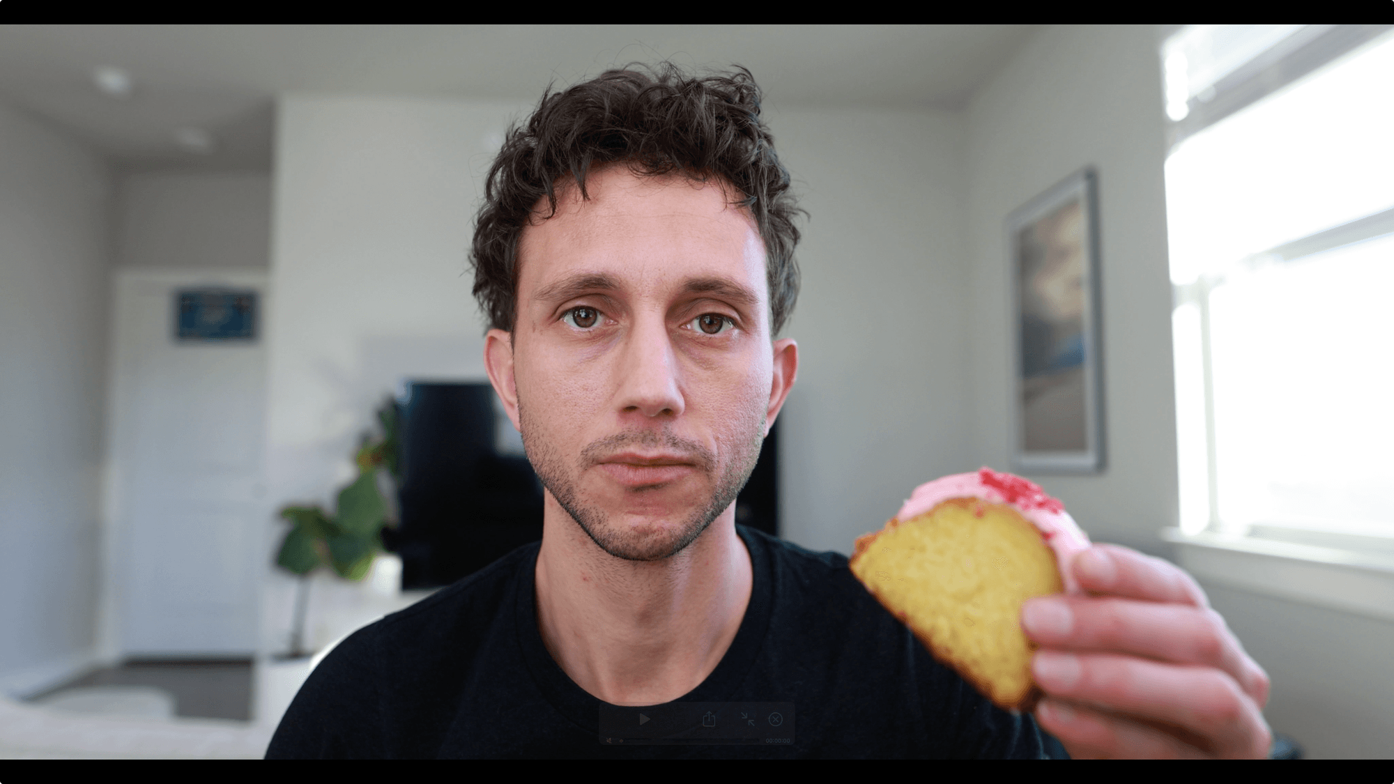 Mark looks into the camera holding a slice of pink-frosted pound cake, a still from a Gonna Eat Bread video.