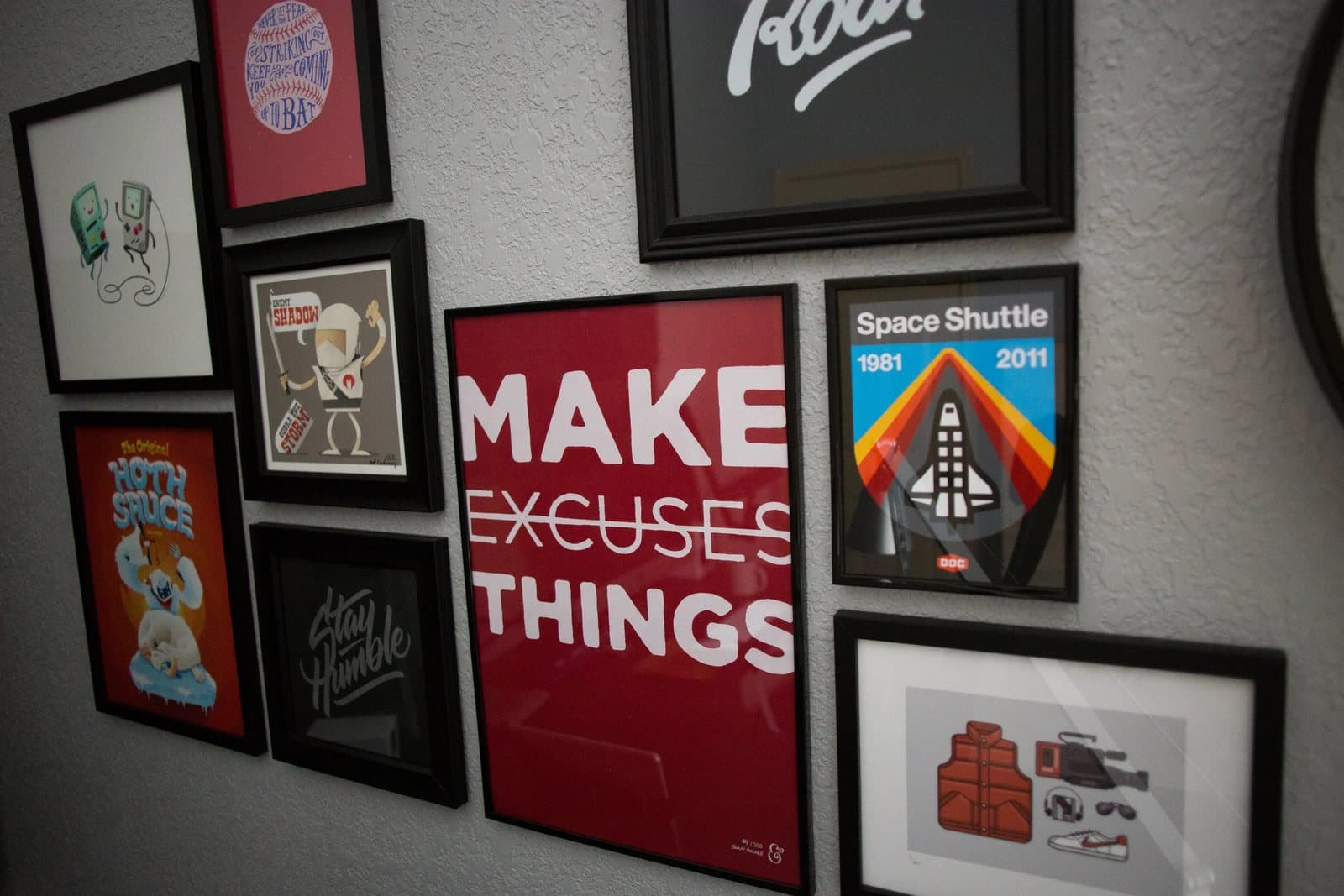 Framed prints on Kyle's studio wall, including a red poster reading Make Things with Excuses crossed out.
