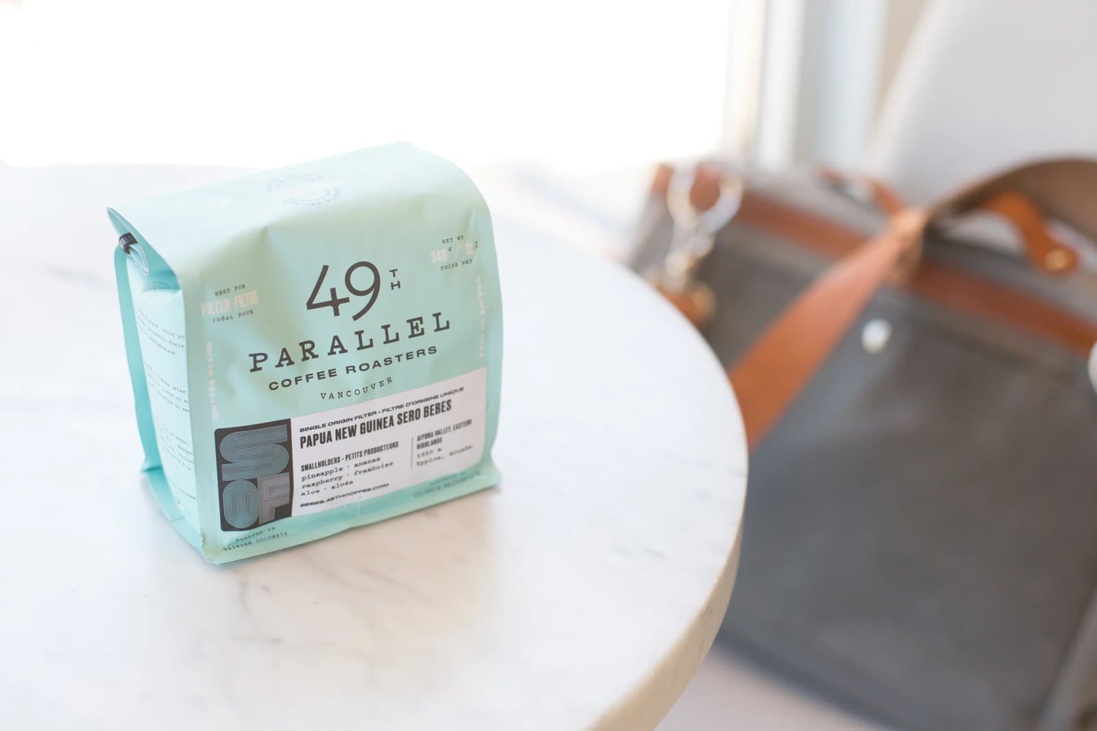 A bag of 49th Parallel coffee sits on a marble cafe table beside Kyle's canvas bag.