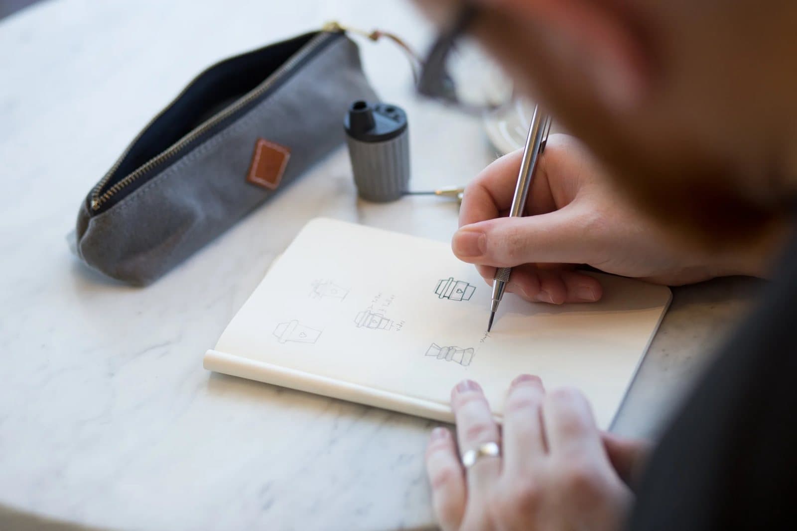 Over Kyle's shoulder, a pencil sketches coffee icons in a notebook on white marble.
