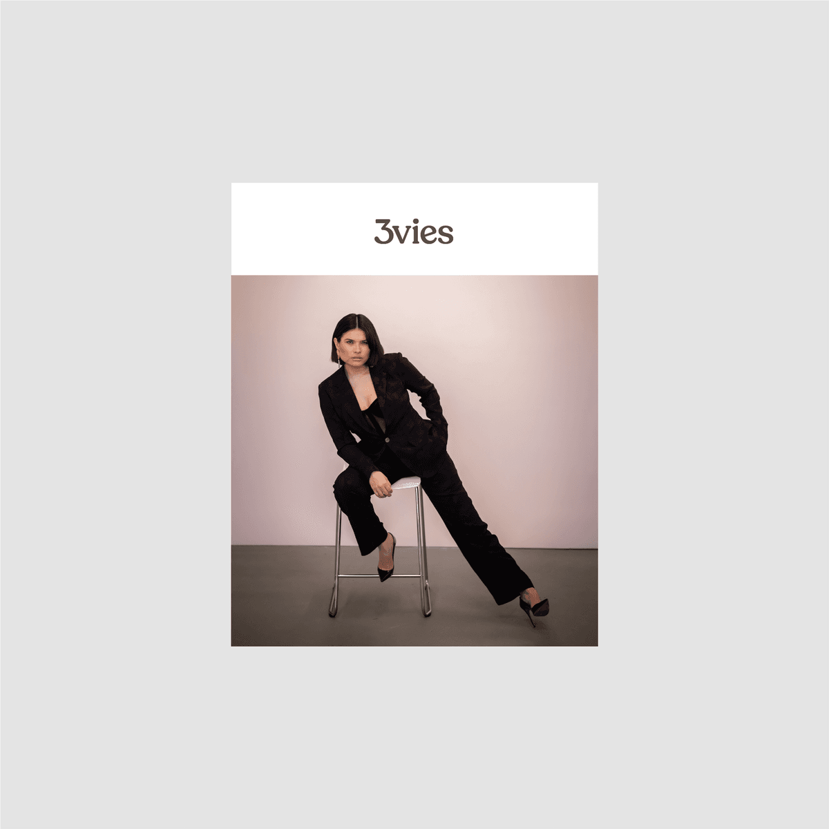 Cover of 3vies Volume 37, a woman in a black suit perched on a stool against a pink wall.