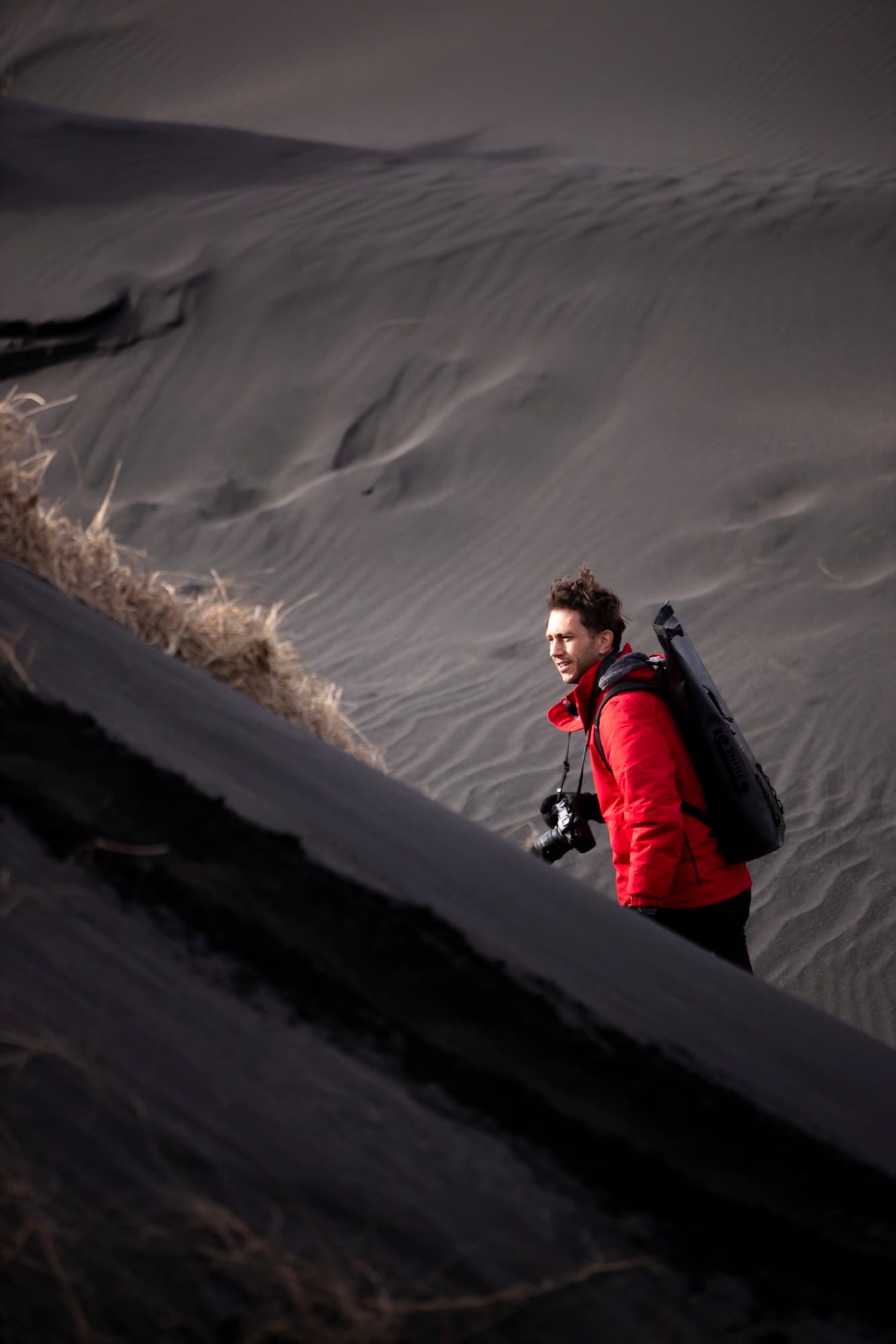 Mark in a red jacket with a camera, climbing a black sand dune in Iceland.