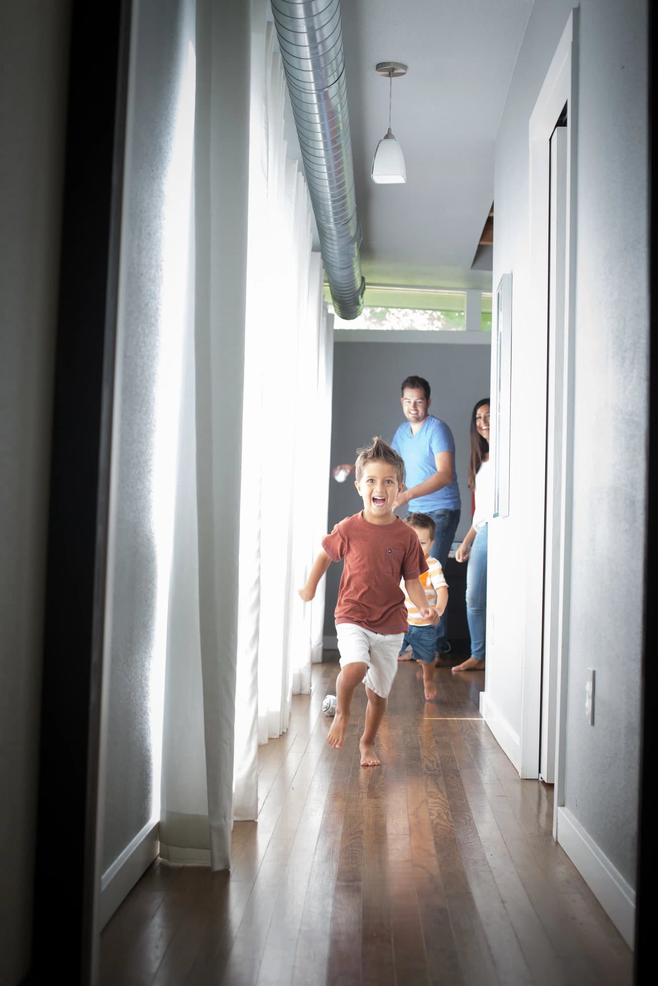 A barefoot boy runs down the sunlit hallway toward the camera as his family follows.