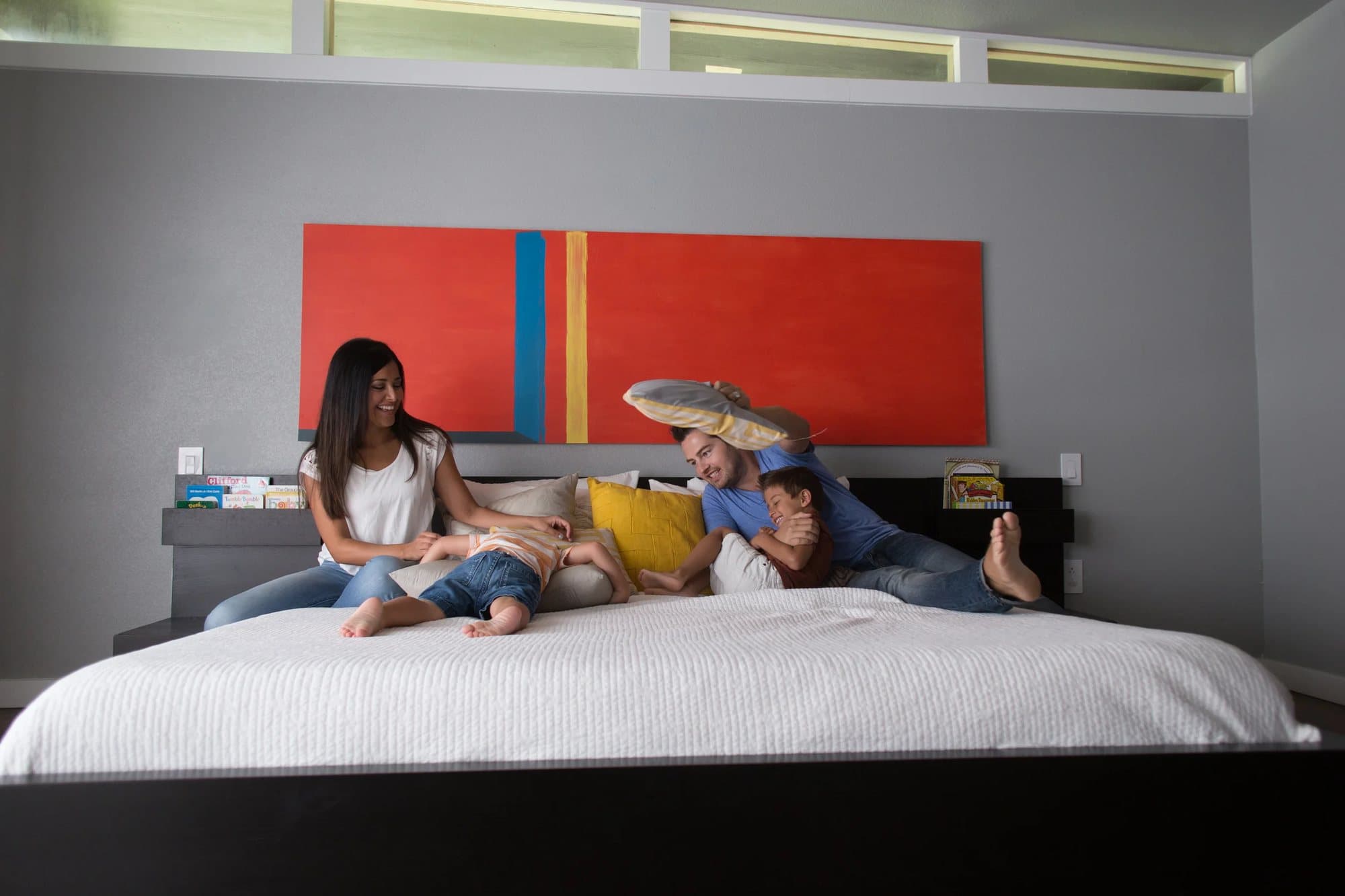 Leila and Nick laugh with their boys piled on the bed under a red and blue painting.