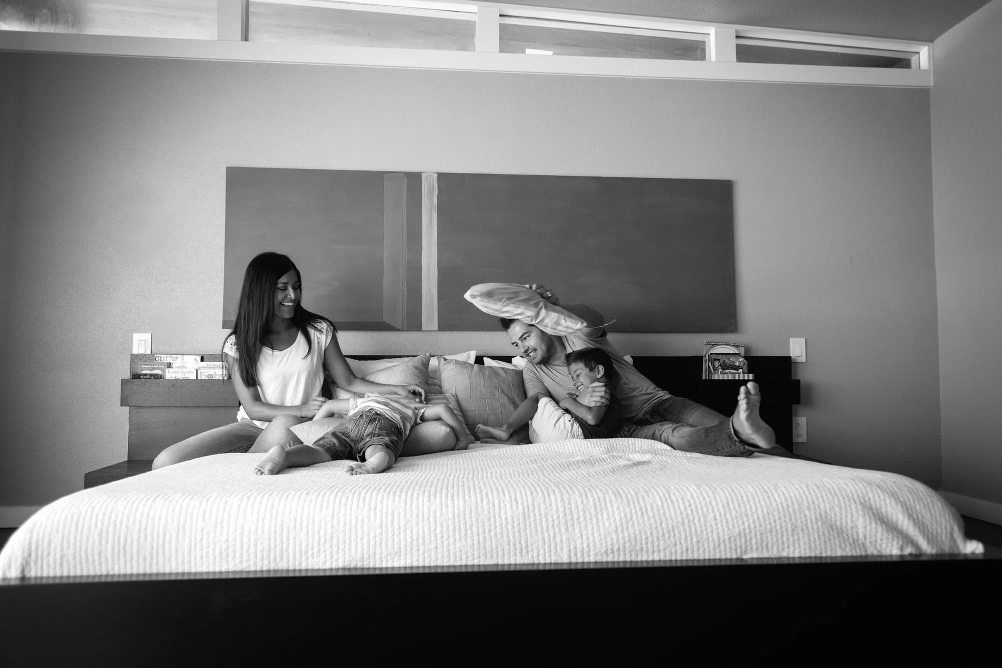 Black and white view of the family tangled together laughing on their bed at home.