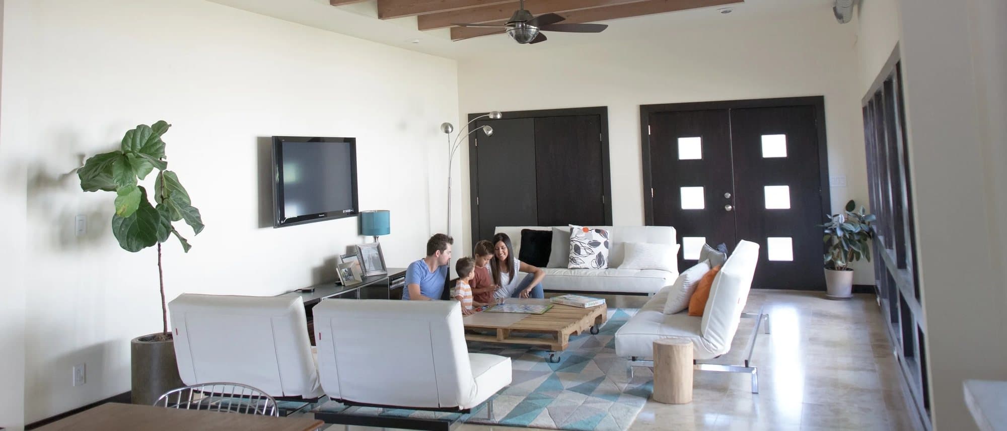 Wide view of the airy, white living room with the family gathered around the coffee table.