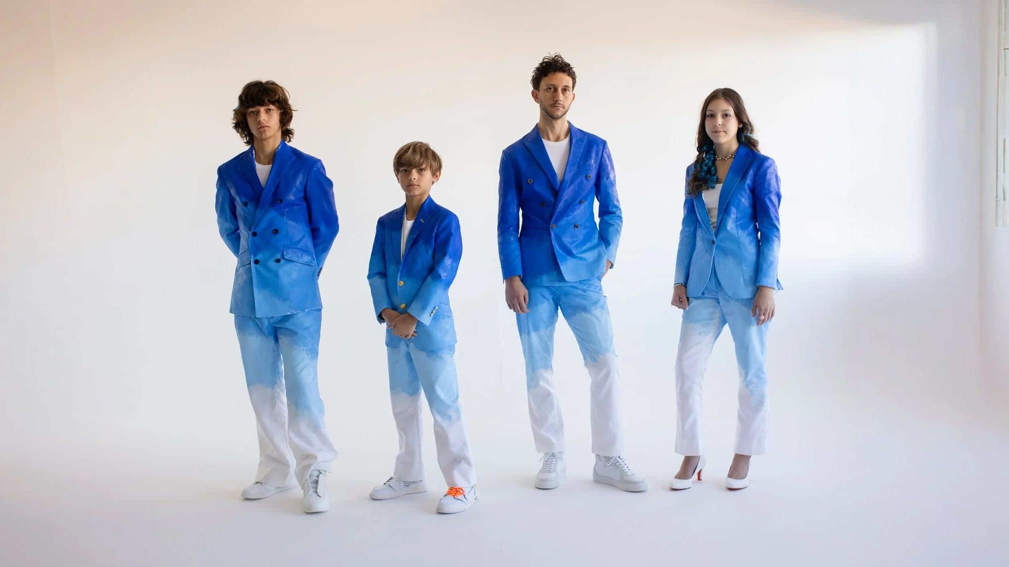 Four people in matching blue-to-white gradient suits stand in a white room, from the TIMELESS exhibit.