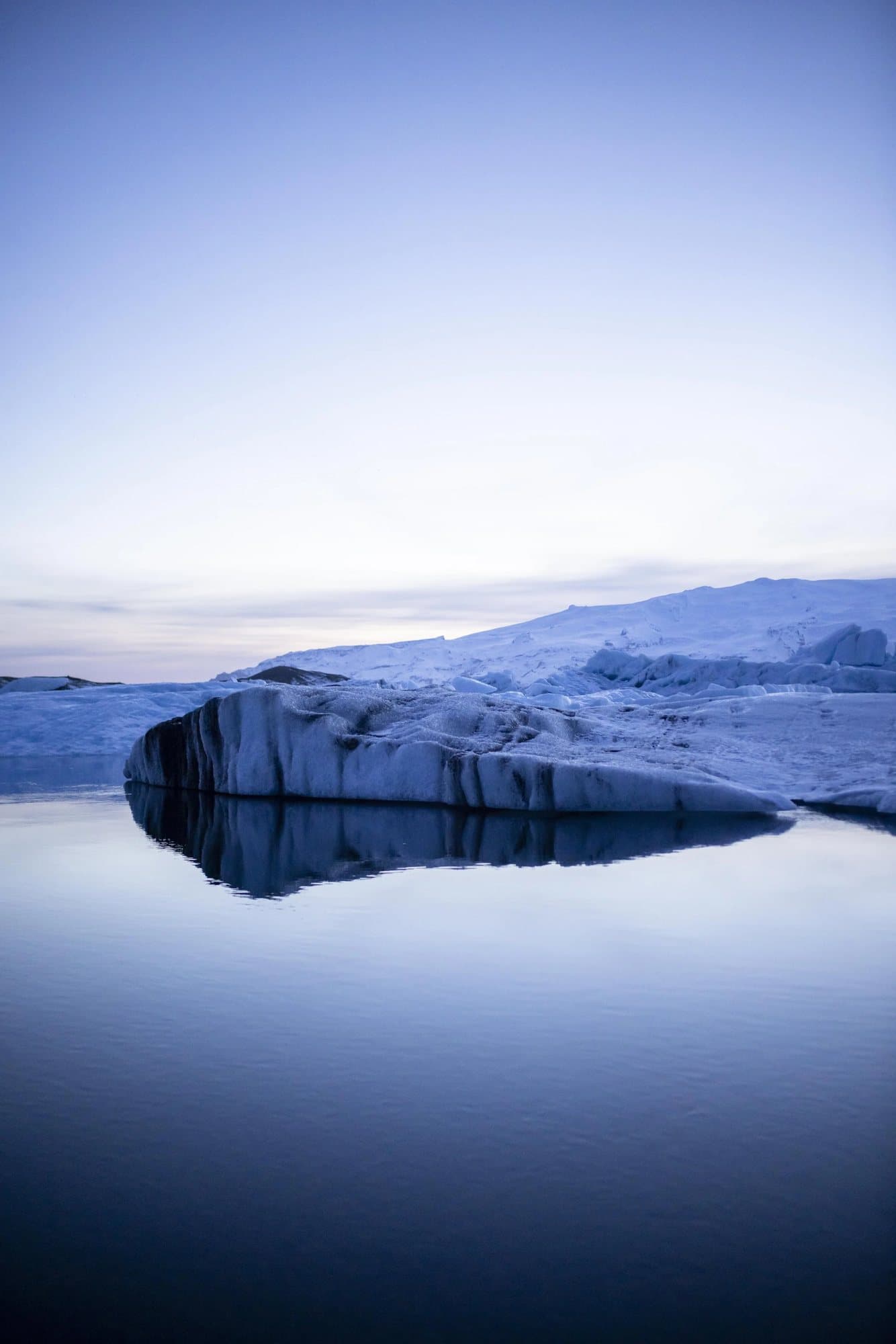 A blue-lit iceberg resting on still, mirror-like water in Iceland.