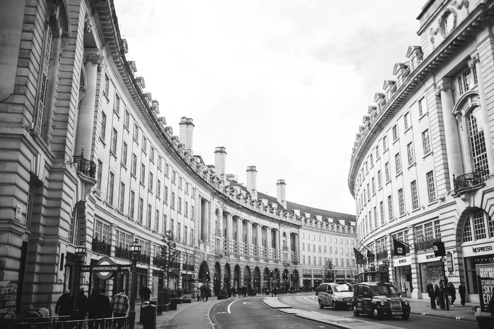 Black and white view of the curving facades of Regent Street in London, with black cabs below.