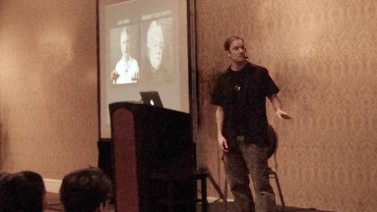 Bret Victor on stage beside a projected slide of two portraits.