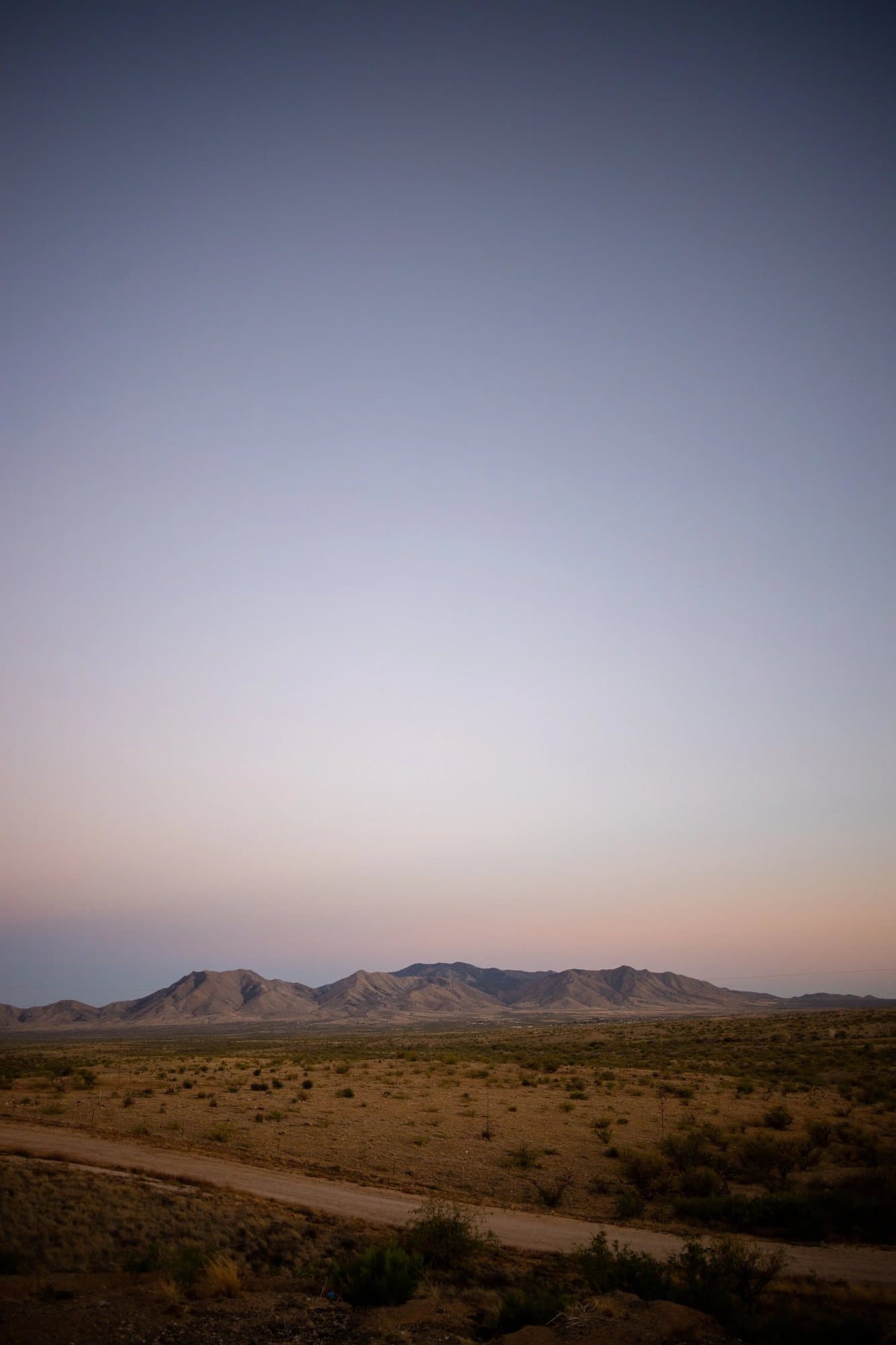 A desert road and distant mountains under a pastel dusk sky in Arizona.