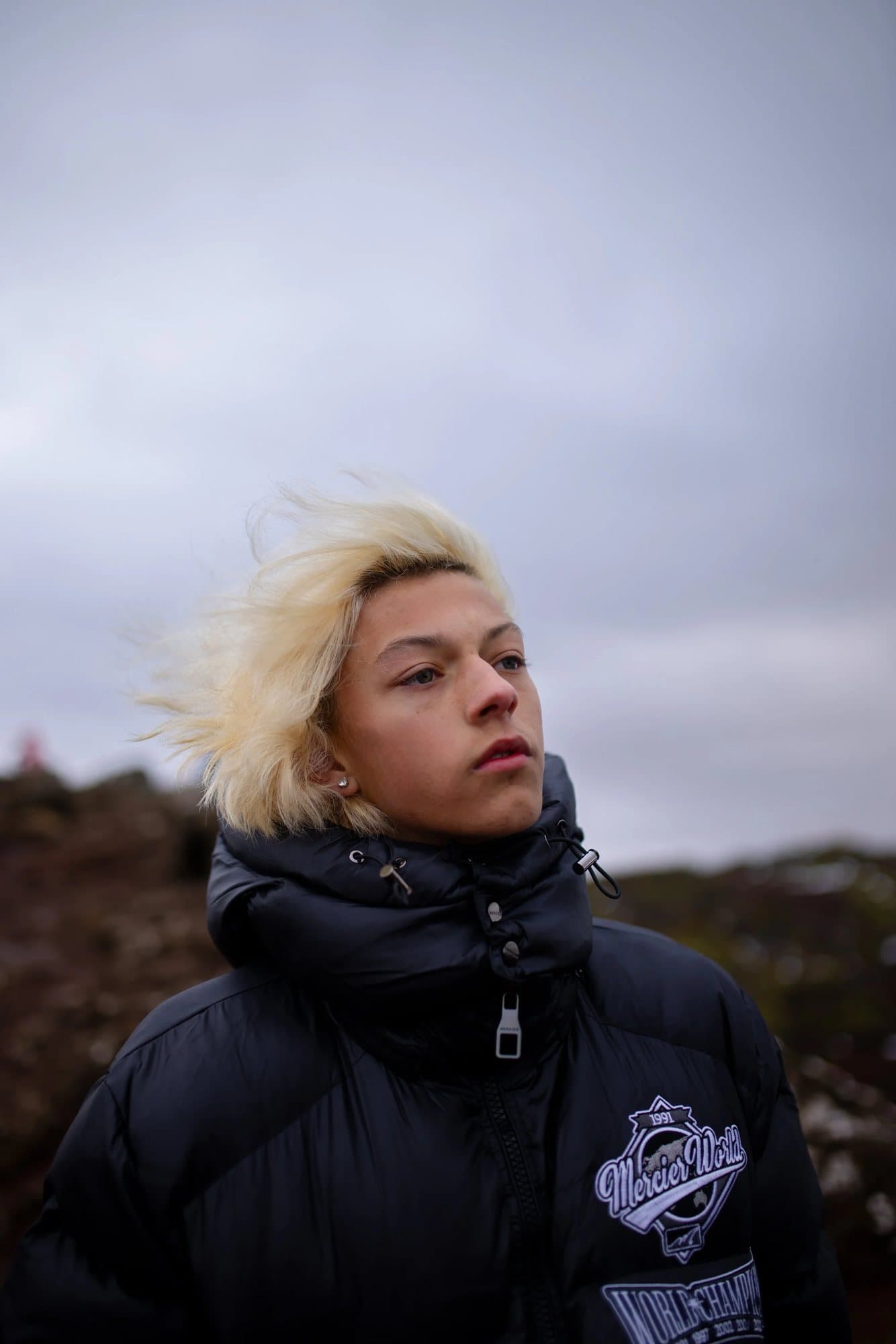Paxman Warnick, featured in Volume 40, with windswept bleached hair in a black puffer jacket in Iceland.