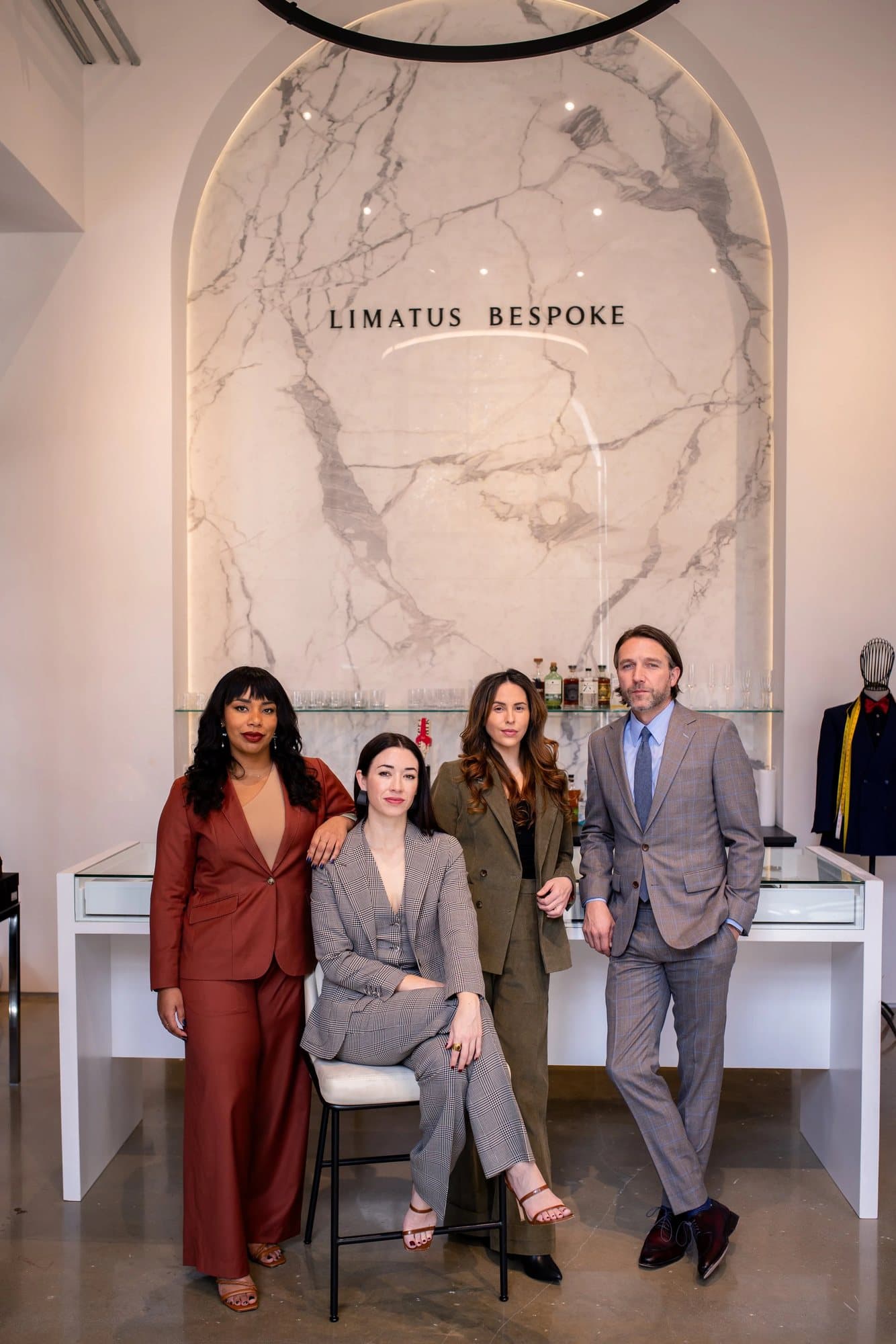 The Limatus Bespoke team, featured in Volume 38, in tailored suits beneath their marble logo wall.