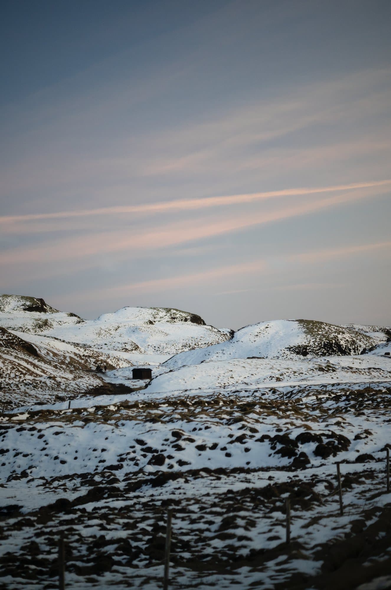 Photo handout of snow-covered Icelandic hills and a small hut under pink streaked clouds.