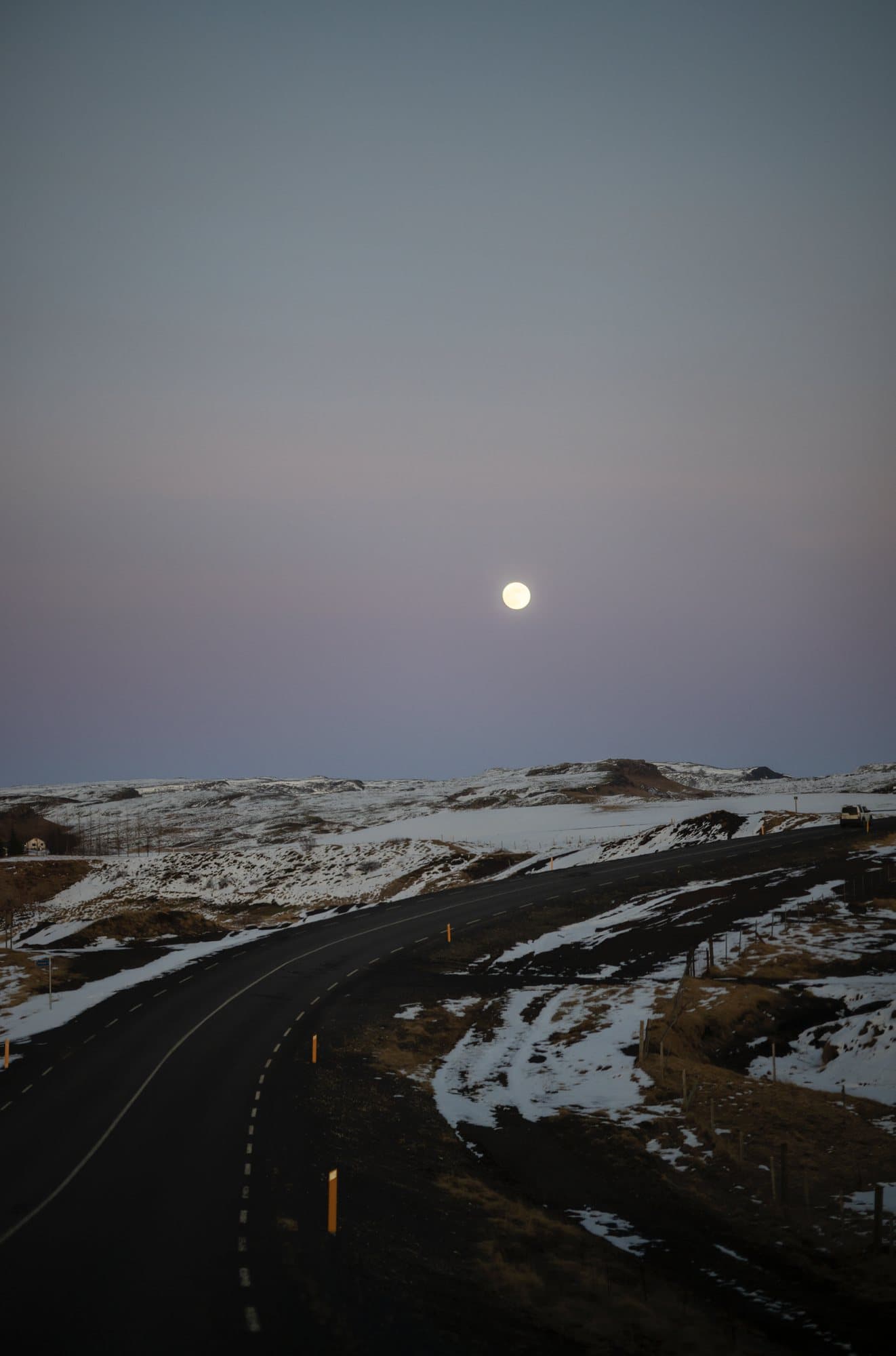 A full moon rising over a winding road through snowy Icelandic hills.