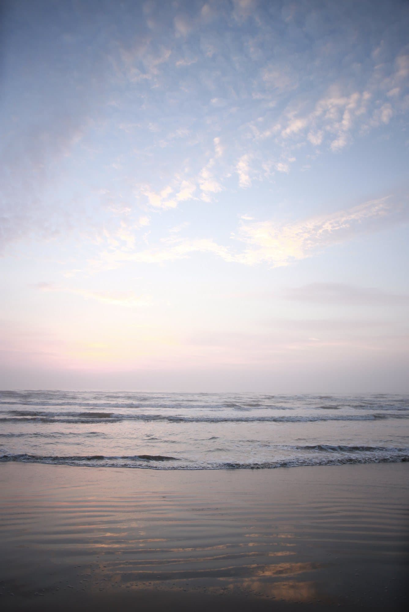 Photo handout of gentle waves on a beach under a pastel sunrise sky.