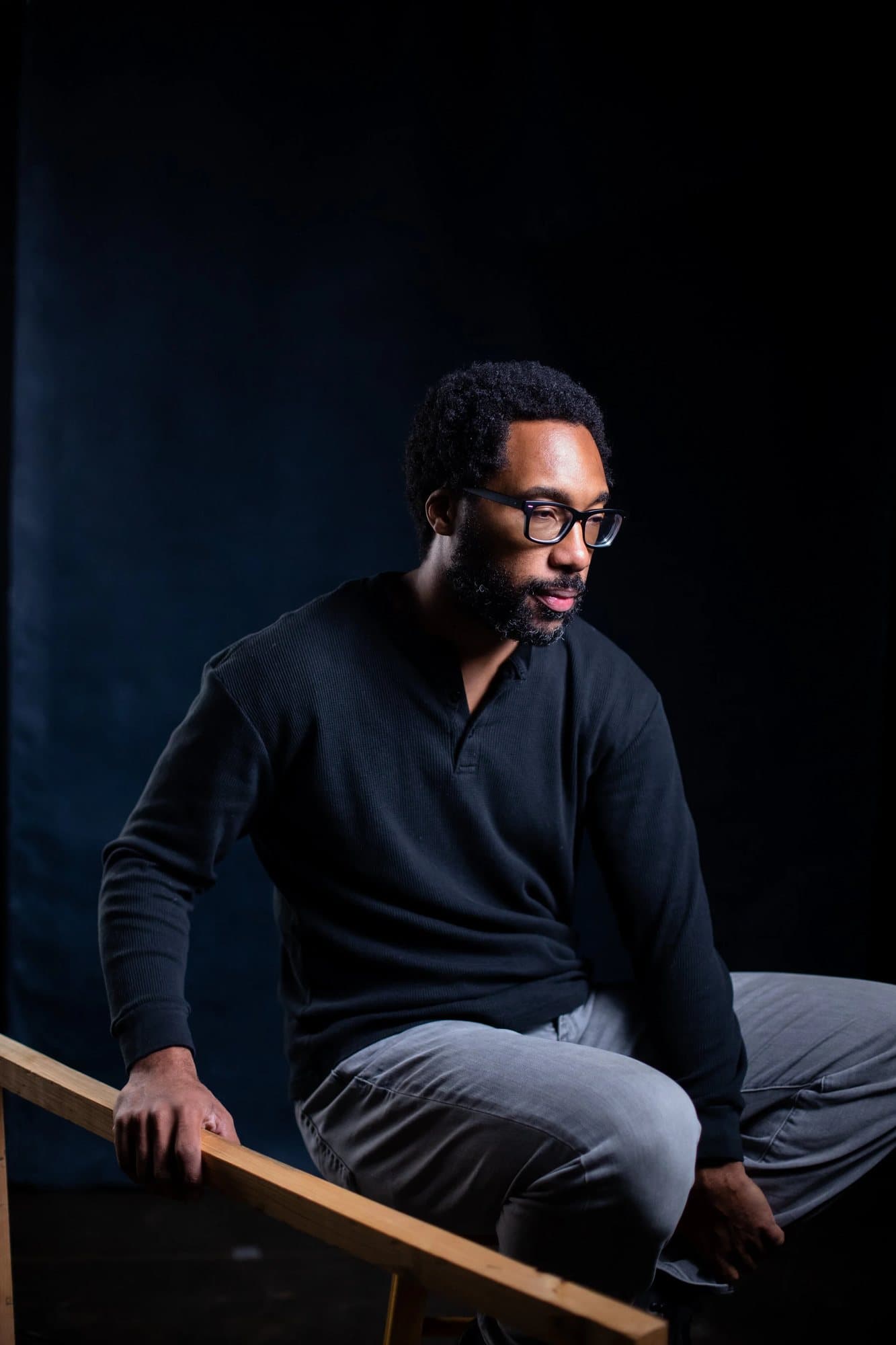 Anthony Francis in glasses and a dark henley, seated against a black studio backdrop.