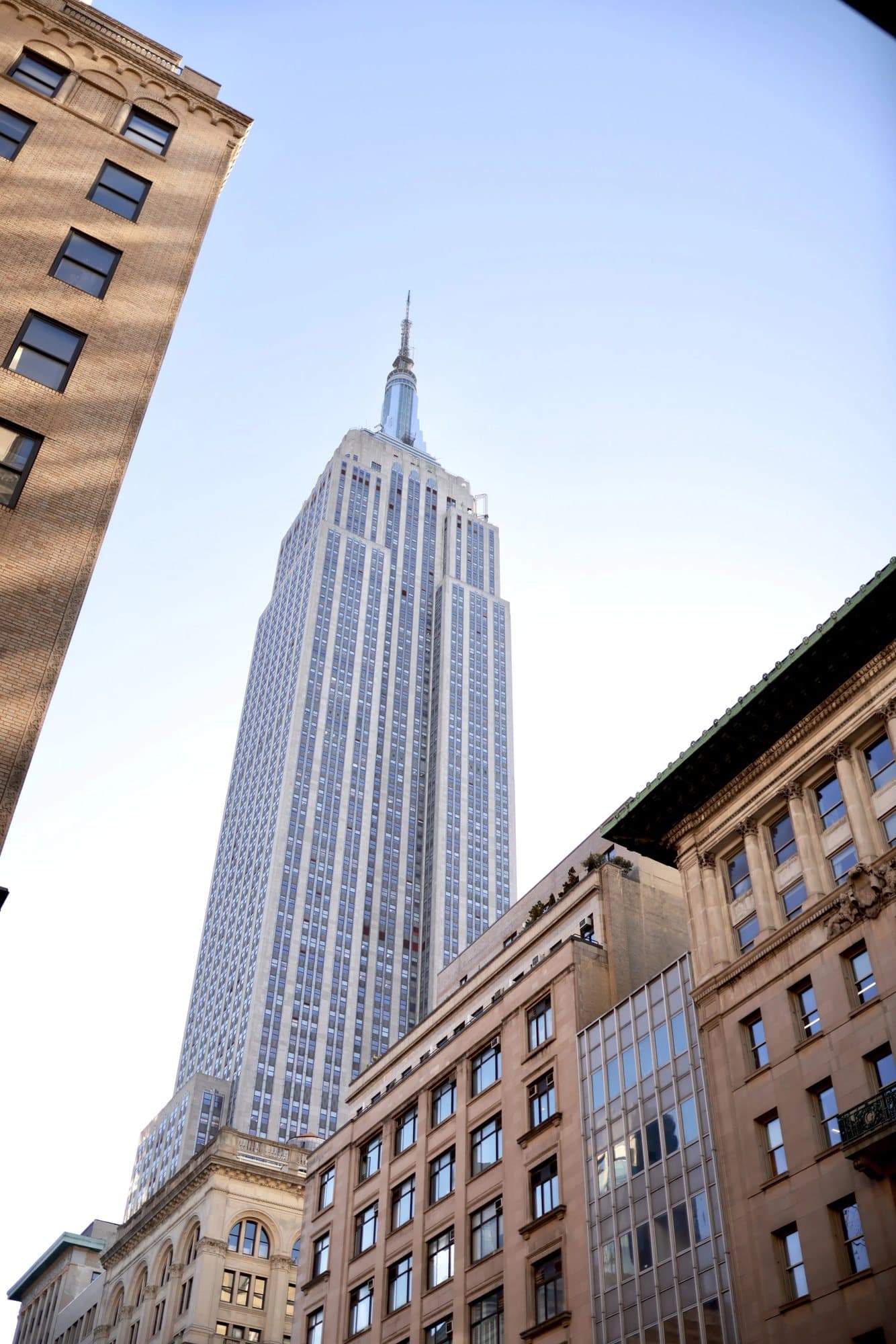 Looking up at the Empire State Building rising above Manhattan buildings.