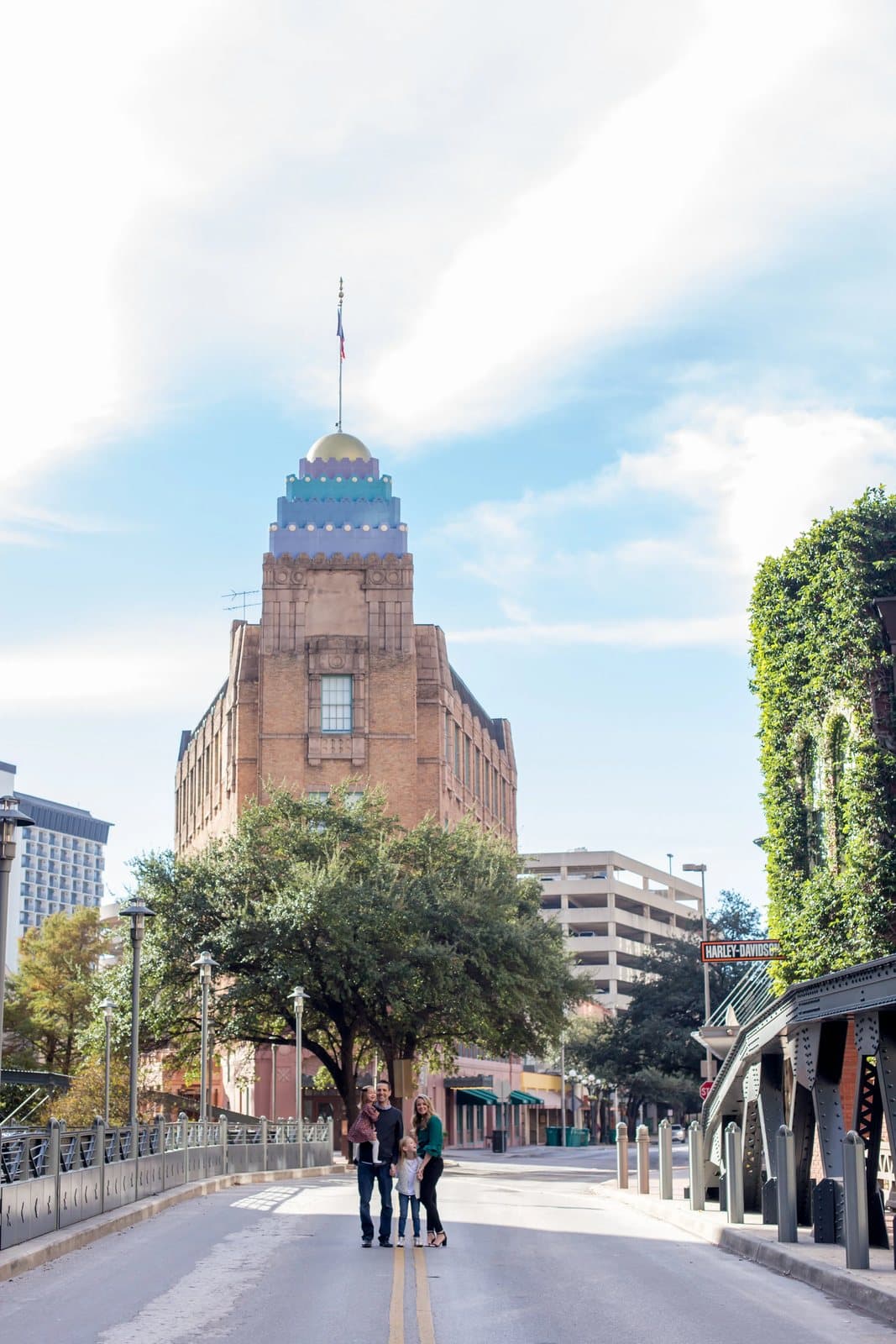 A family stands on a San Antonio street before a historic tiled-dome tower under a bright sky.