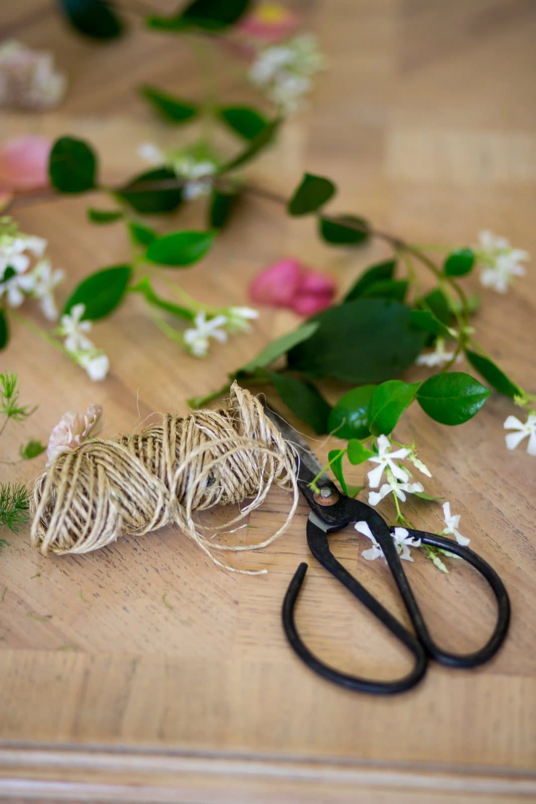 Twine, black scissors, and scattered jasmine and roses on a wood table, a Mother's Day styling detail.