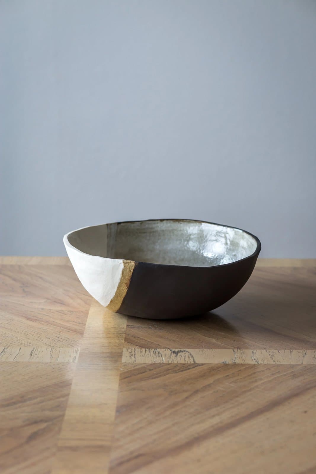 A handmade ceramic bowl, half white and half black, on a wood table against a pale blue wall.