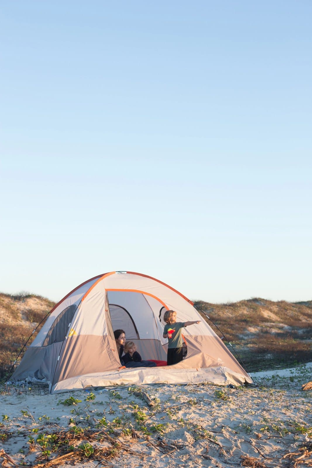 Children peek out of a dome tent pitched among grassy sand dunes on Mustang Island.