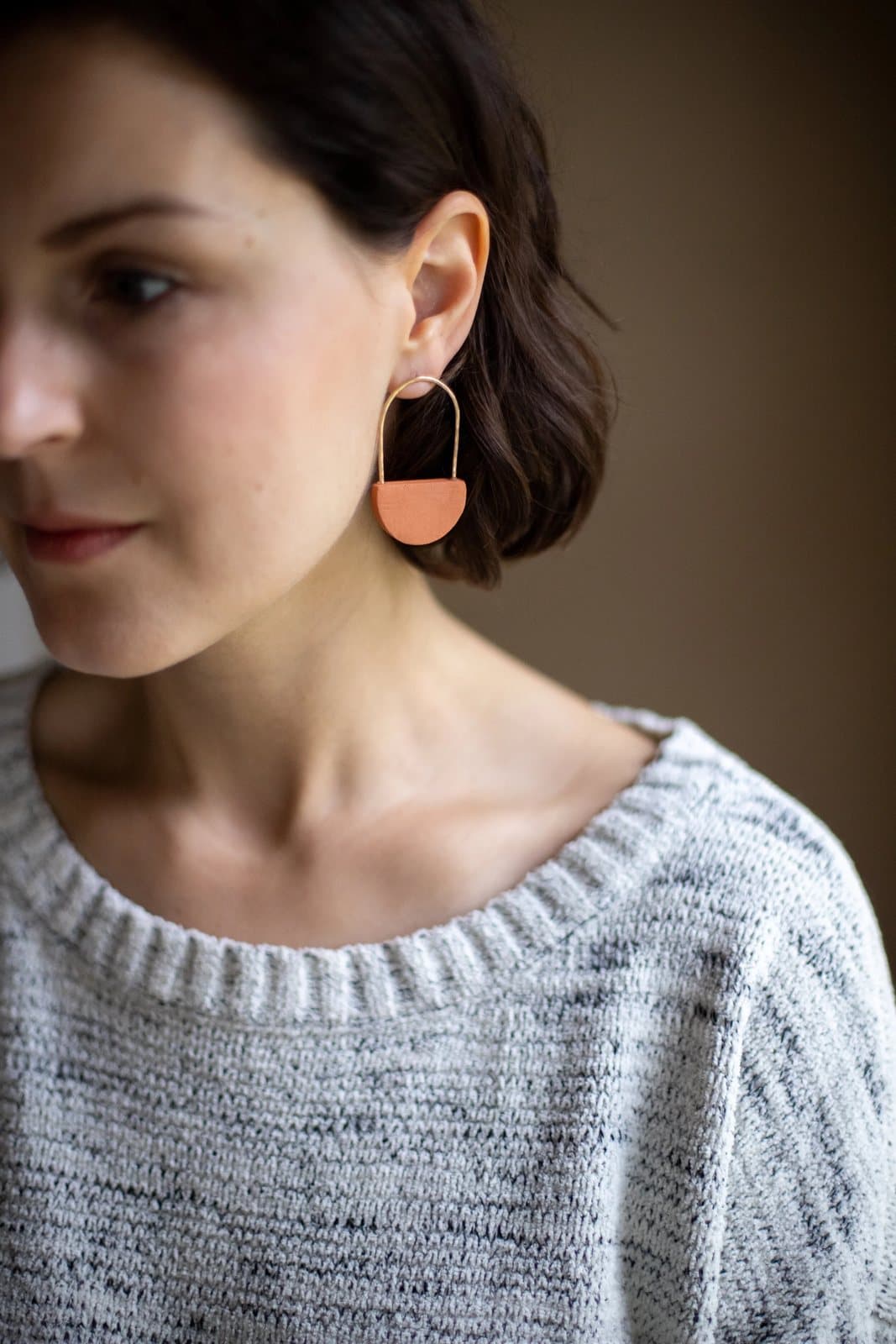 Close portrait of a woman in a knit sweater wearing a copper half-moon earring.