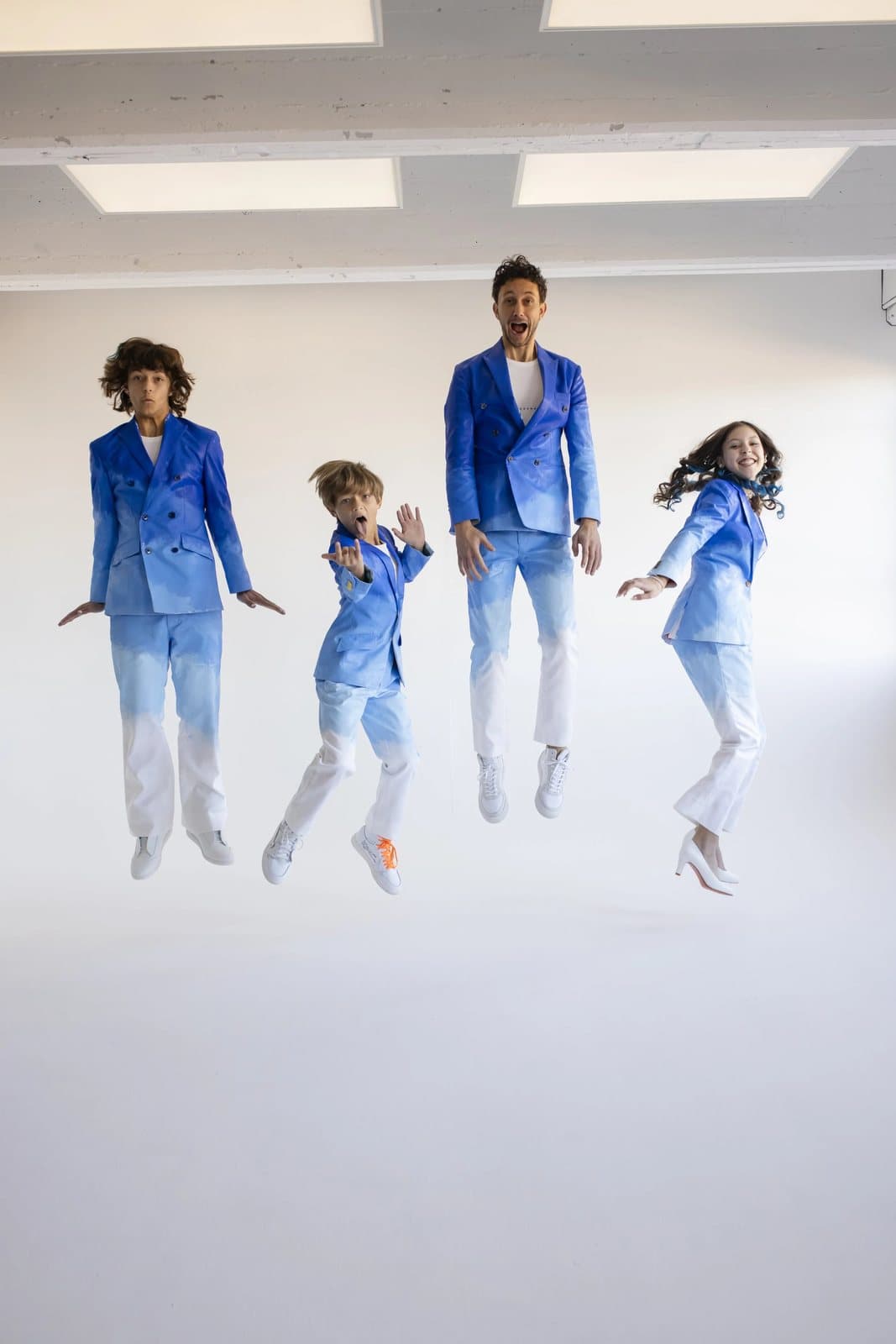 Four people in blue-to-white gradient suits jump in a white studio, from the TIMELESS shoot.