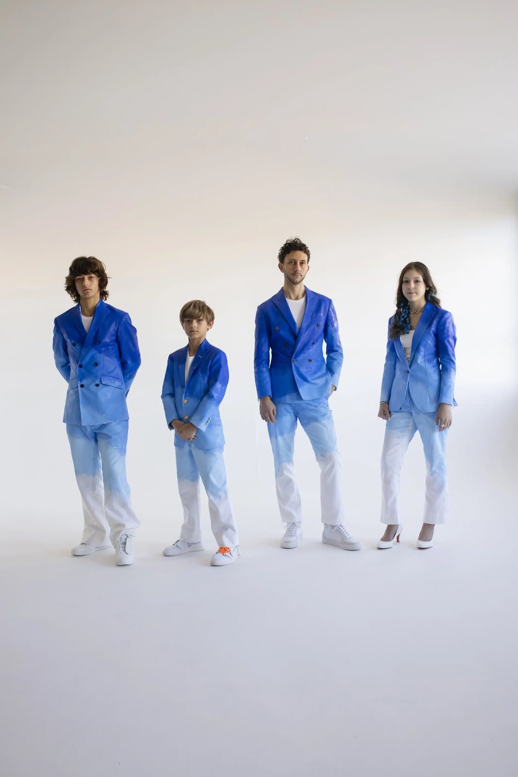 Four people in blue-to-white gradient suits stand in a row in a bright white studio.