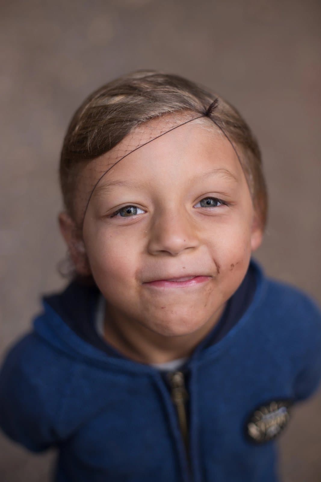 Close portrait of a smiling boy with a smudged face and a blue hoodie.