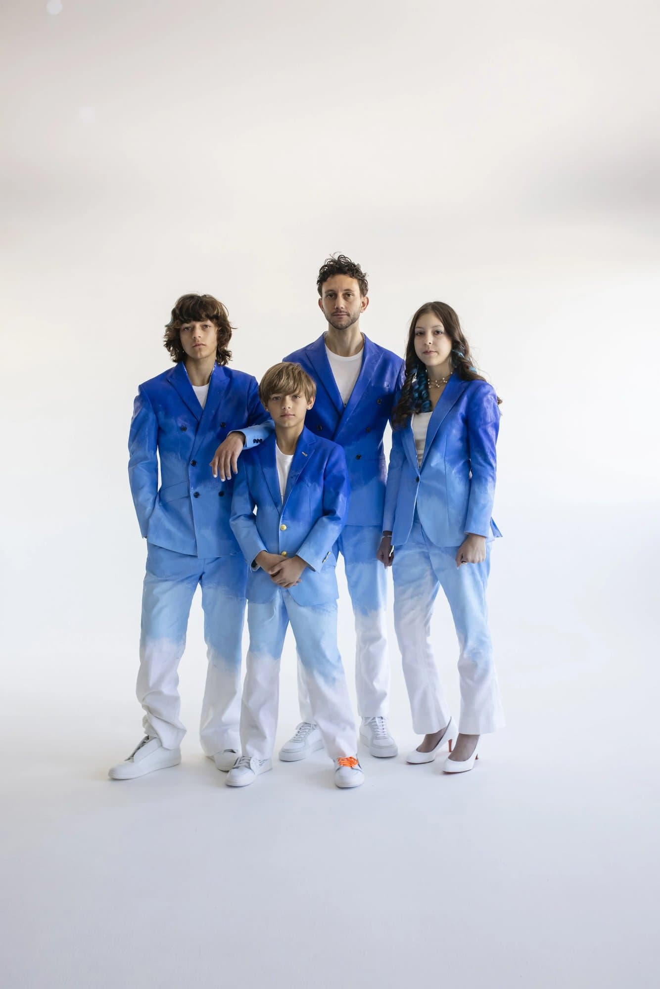 Mark and his three children standing together in matching hand-painted blue and white suits against a white backdrop.