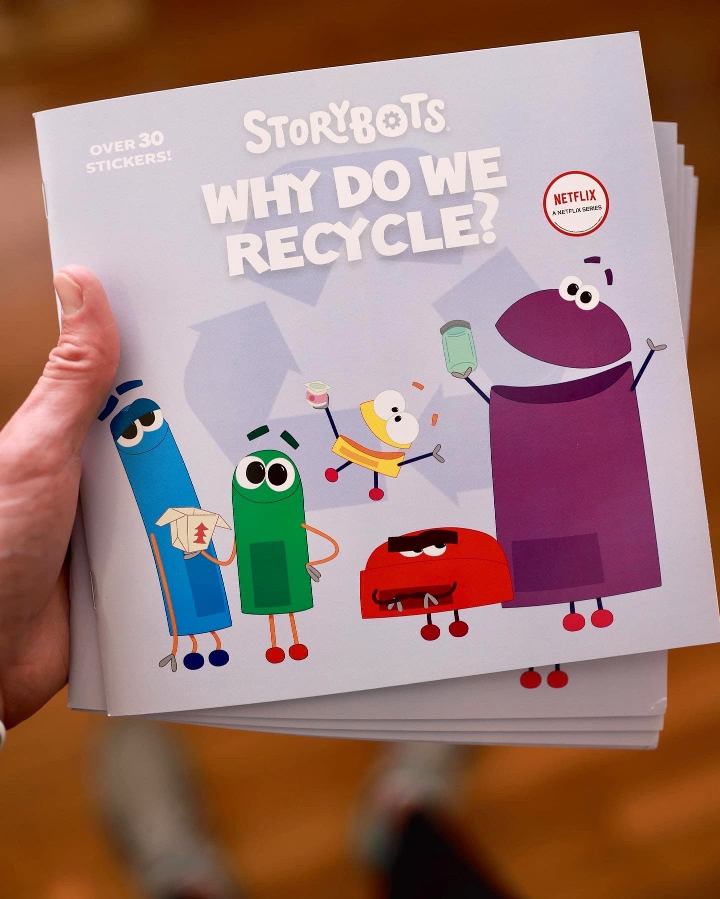 A hand holding a stack of the StoryBots picture book Why Do We Recycle?