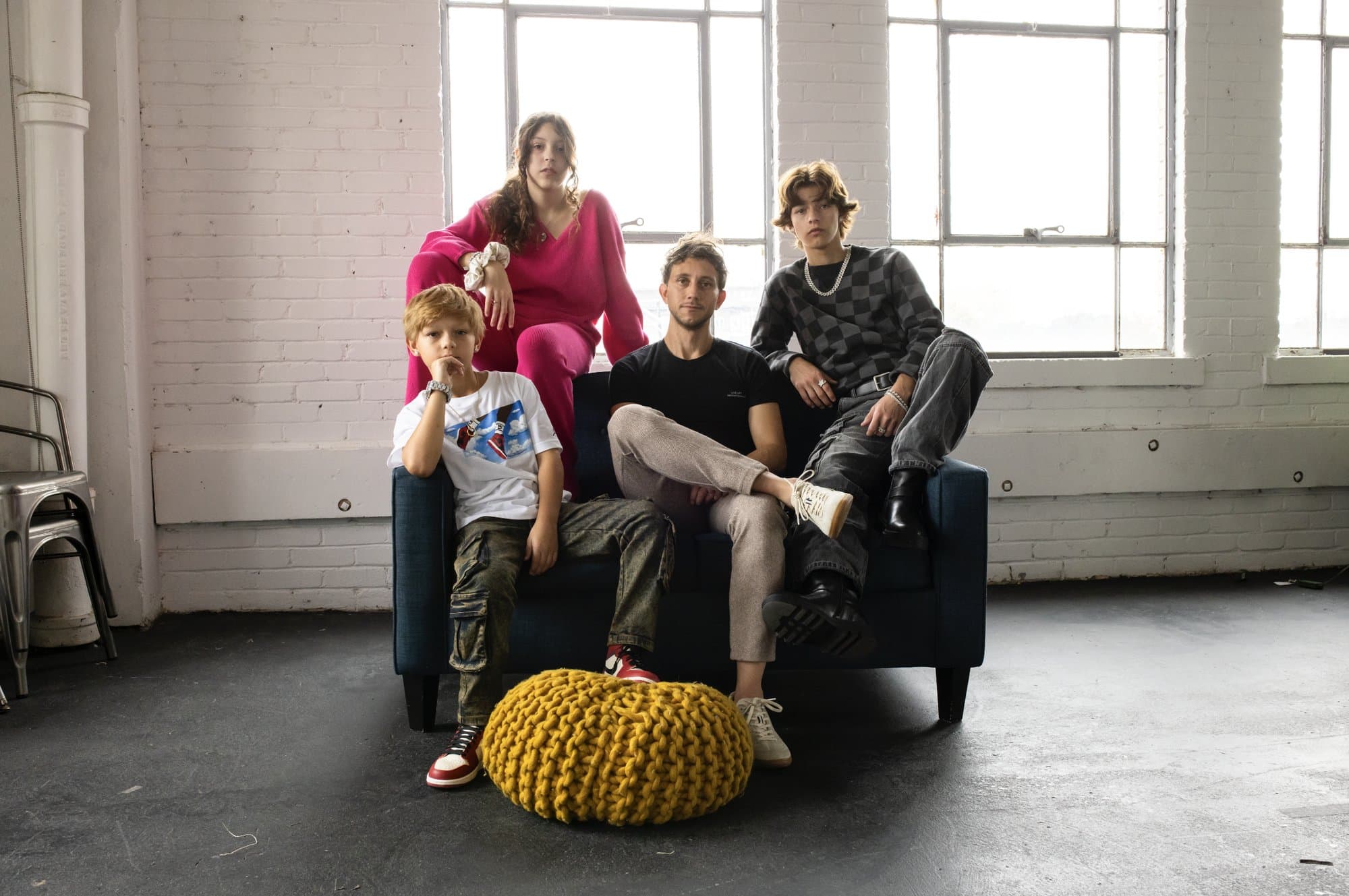 Mark and his three children posed together on a sofa in a bright loft studio with tall windows.